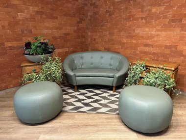 Modern bir açık yeşil deri kanepe, tuğladan duvarları olan rahat bir yerde göze çarpar. Geniş saksı bitkileri mobilyaların etrafını sararken, dairesel puflar da dekoru güçlendirir. Atmosfer sıcak, rahatlamak için mükemmel..