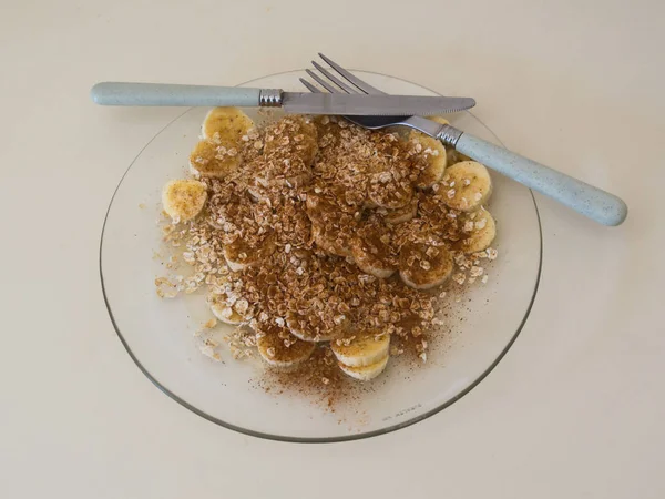 Healthy and tasty snack, plate of sliced bananas with oats, sugar, cinnamon. Cutlery crossed.