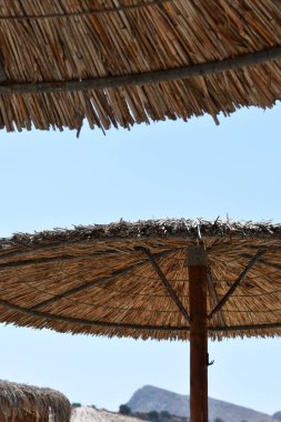 Rodos adasındaki Stegna plajı, saman şemsiyeli. Yunanistan 'da kumlu bir sahilde kadife şemsiyeler. Yunanistan 'da tatiller. Rodos 'a git. Açık kumsal şemsiyeleri. Yaz ve tatiller. 