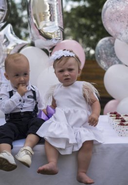 Erkek ve kız kardeşler, ikizler ilk doğum günlerini kutlarlar. Balonların arka planına karşı giyinmiş, yan yana oturuyorlar. Çocuklar dışarıda parti veriyor. İlk doğum gününde tatlı küçük prenses.