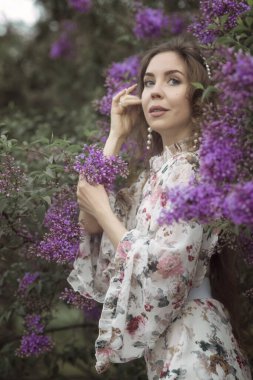 Güzel bir kadının portresi ilkbaharda pembe çiçeklerin yumuşak, taze ve doğal kokusunu içine çekiyor. Yumuşaklığın kişileştirilmesi, sofistike olmak, saflık. Mor çiçekli pembe elbiseli kız.