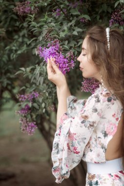 Çiçek açan leylakların arasında ince bir kadın. Uzun siyah saçlı, romantik bir yaz imajı var. Güzel bir kadın bahar aylarında pembe çiçeklerin yumuşak, taze ve doğal kokusunu içine çekiyor.