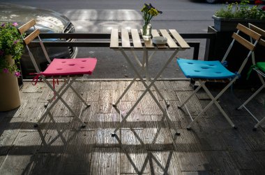 Sabahları, güneş ışığında, sokak kafeteryasında. Boş teras, parlak sandalyeler ve masanın üzerinde cam şişeler içinde yabani çiçekler. Bir Avrupa şehrinde masalı teras ziyaretçileri bekliyor. Yüksek kaliteli fotoğraf..