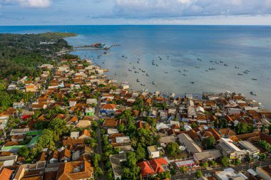 Renkli evleri, yemyeşil otlakları ve suda balıkçı tekneleri olan bir sahil köyünün havadan görünüşü.