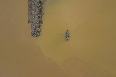 Çamurlu bir nehirde kayalık bir toprak setinin yanında küçük bir teknenin havadan görüntüsü..