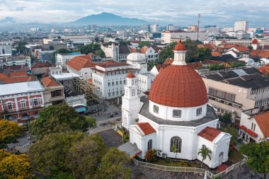 Tarihi mimarisi olan bir şehrin havadan görünüşü, arka planda modern binalar ve dağlarla çevrili, kırmızı kubbeli önemli bir beyaz kilisenin görüntüsü.