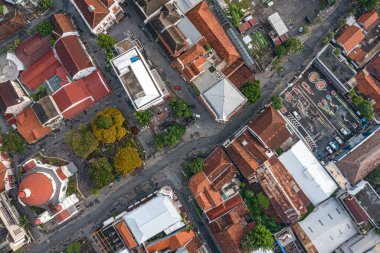 Kırmızı çatılı binalar ve ağaçlarla kesişen şehir manzarası.