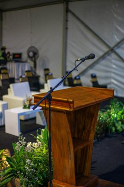Çadırda bitki ve sandalyelerle çevrili, mikrofonlu ahşap bir podyum.