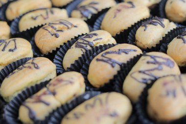 Çikolata çiselemeli çeşitli hamur işlerinin yakın plan görüntüsü, siyah kağıt bardaklara dizilmiş.