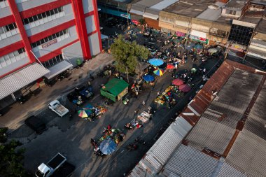 Renkli şemsiyeli, satıcı ve binalarla çevrili insanların alışveriş yaptığı hareketli bir sokak pazarının havadan görüntüsü.