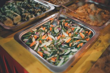 Havuç, salatalık ve yeşil fasulye gibi renkli sebzelerden oluşan canlı bir karışım, metal bir tepside sergileniyor, taze ve sağlıklı bir yemek sergileniyor.