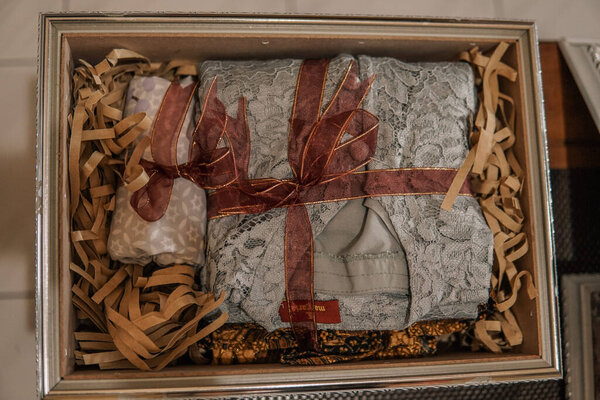 A beautifully wrapped gift box containing lace clothing and decorative items, surrounded by shredded paper filler
