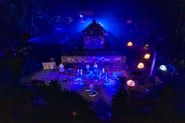 Renkli ışıklarla aydınlatılmış, geleneksel giyinmiş müzisyen ve dansçıların yer aldığı tarihi bir yerde gece kültür gösterisi.