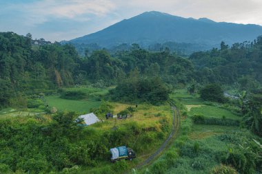 Ağaçlar ve tarlalarla çevrili bir çadır ve aracın yer aldığı yemyeşil bir manzaranın manzarası.