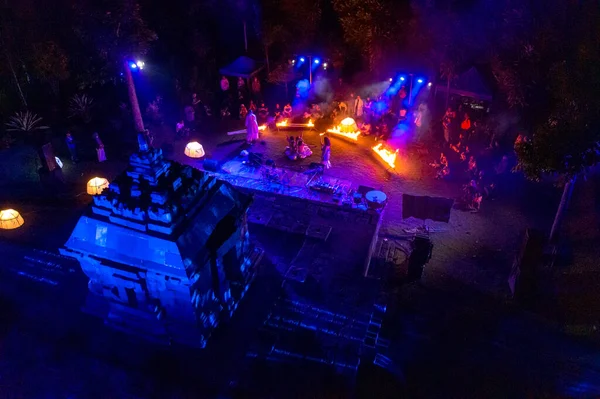Gece vakti, bir tapınak, ateş çukurları ve mavi ışık altındaki sanatçılarla yapılan kültürel bir olayın havadan görüntüsü.