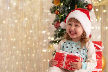 Pijama ve Santa şapka mutlu, küçük bir kız bir hediye aldı. Noel tatil atmosferi mutluluk eve getirdi. hediye kutuları saten kurdeleler ile bağlı. Noel ağacı garland kurutulmuş portakal ve topları ile süslüdür