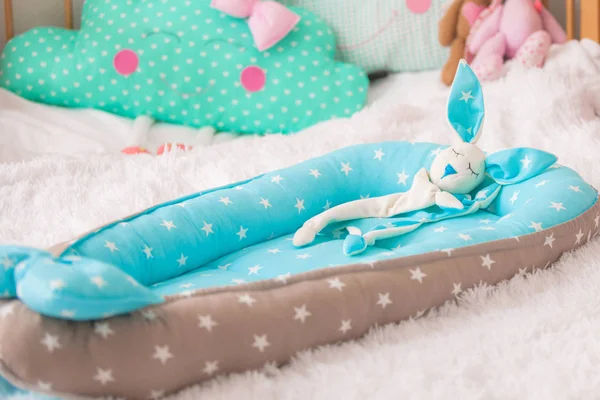 Rabbit Comforter. designer cocoon for baby in the form of cradle. in the background, a cloud-shaped pillow and children\'s toys. in the cradle lies a stitched hare Comforter toy for better baby sleep