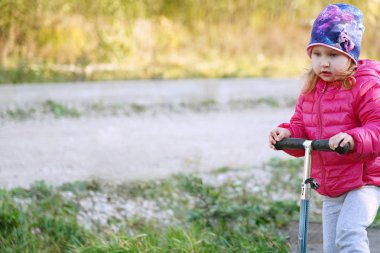 scooter tanıtıcısı tutan kız. bir scooter sürme ilk deneyimi. serin hava bebek sıcak giyindi. kendi başlarına kullanmayı öğrenme. alan metni için çocuğun önünde bir sürü