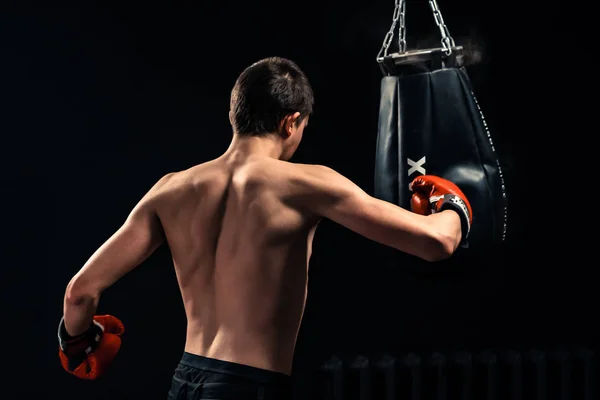 Ragazzo che colpisce il sacco da boxe su sfondo scuro — Foto Stock