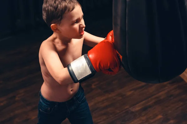 Chico golpeando el saco de boxeo sobre fondo oscuro. la agresión — Foto de Stock