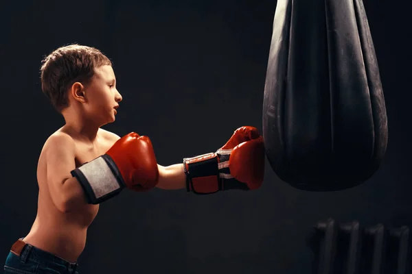 Ragazzo che colpisce il sacco da boxe su sfondo scuro. l'aggressività — Foto Stock