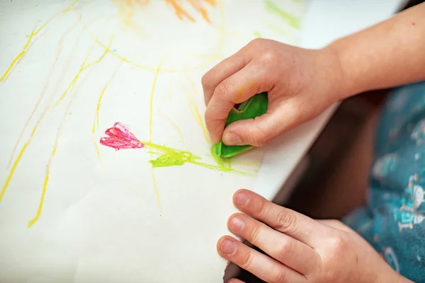 the child draws a flower on paper with wax crayons made with his