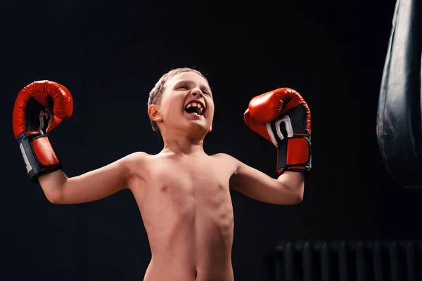 Un chico cerca de un saco de boxeo en guantes de boxeo grita y levanta hola — Foto de Stock