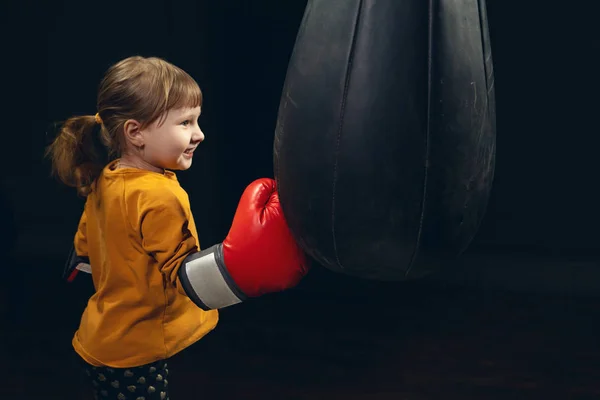 Bambina che colpisce un sacco da boxe su uno sfondo scuro. aggressione — Foto Stock