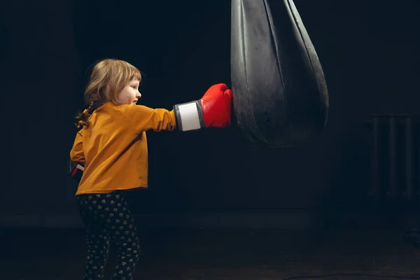 Bambina che colpisce un sacco da boxe su uno sfondo scuro. aggressione — Foto Stock