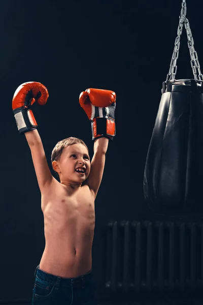 Un ragazzo vicino a un sacco da boxe in guanti da boxe urla e solleva ciao — Foto Stock