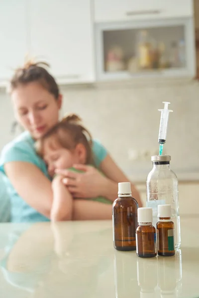 テーブルの上の医学。女性は子供を保持して、慎重に彼女に子供を押します。病気による体調不良を感じてください。薬の瓶に焦点を当ててください。 — ストック写真