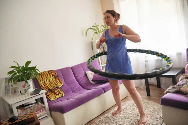 Una mujer se convierte en un aro hula en casa. autoentrenamiento con un aro . — Foto de Stock