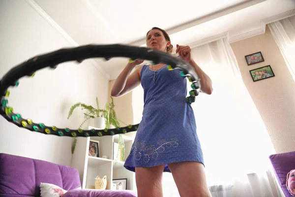 Una mujer se convierte en un aro hula en casa. autoentrenamiento con un aro . — Foto de Stock