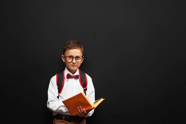 Радостный маленький мальчик стоит на черном фоне с книгой в привет — стоковое фото