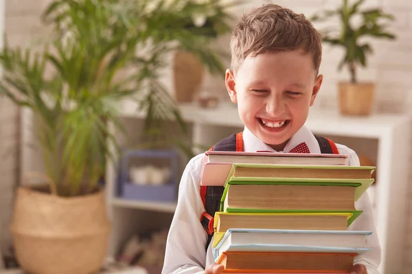 Jongen student houdt een grote stapel boeken en glimlacht gelukkig. — Stockfoto