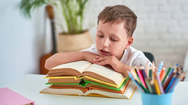 Радостный маленький мальчик сидит за столом с карандашами и учебником — стоковое фото