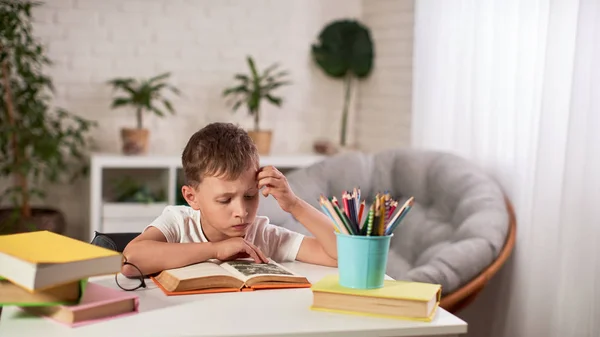 Niño alegre sentado a la mesa con lápices y libro de texto —  Fotos de Stock