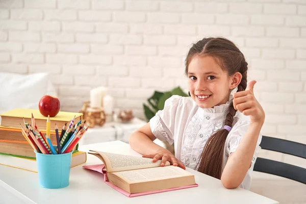 Радісна маленька дівчинка сидить за столом з олівцями і текстбу — стокове фото