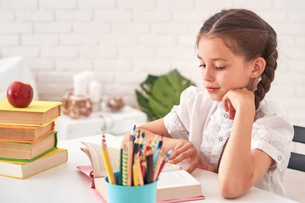 Joyful liten flicka sitter vid bordet med blyertspennor och textboo — Stockfoto