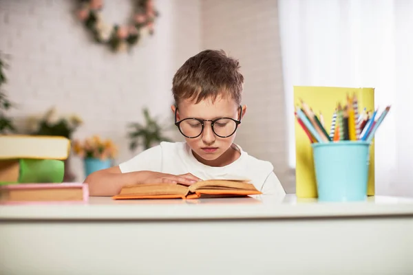 Gioioso bambino seduto a tavola con matite e libro di testo — Foto Stock