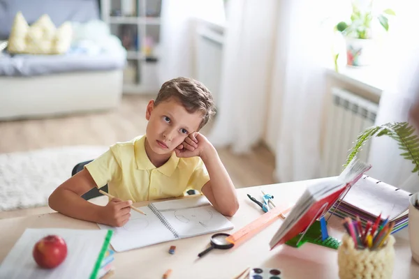 Вдумчивый ребенок сидит за столом с учебниками и учебниками — стоковое фото