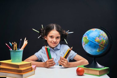 neşeli küçük kız kalem ve textboo ile masada oturuyor