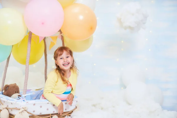 Baby flicka som sitter på ett moln bredvid en korg med ballong i — Stockfoto