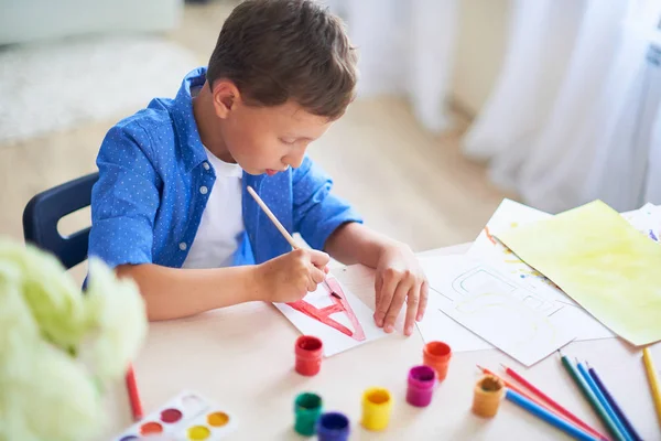 Il bambino disegna con una spazzola vernici ad acquerello su carta il lett — Foto Stock