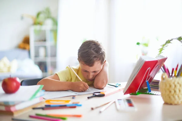 Niño alegre sentado a la mesa con lápices y libro de texto —  Fotos de Stock