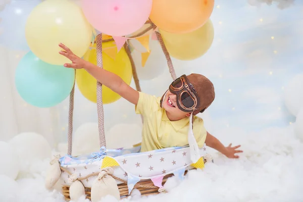 Un niño pequeño se sienta en una canasta de globos en las nubes, fingiendo —  Fotos de Stock