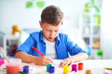 Çocuk kağıt üzerinde bir fırça suluboya boyaları ile çizer lett