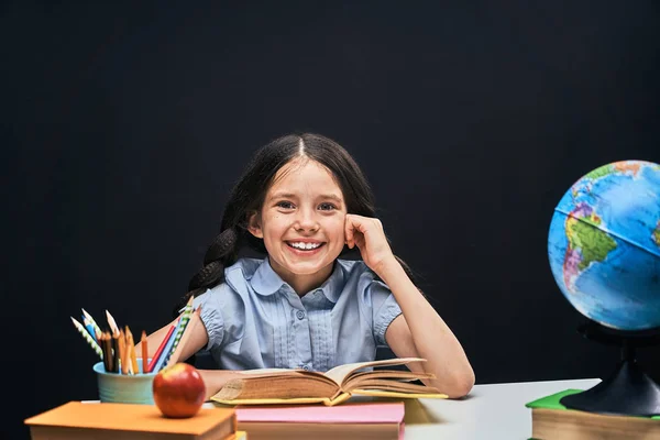 Niña alegre sentada a la mesa con lápices y libros t — Foto de Stock