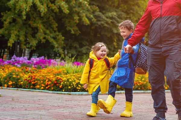 Діти щасливі з радістю сміються йдуть до школи, одягнені в плащі — стокове фото