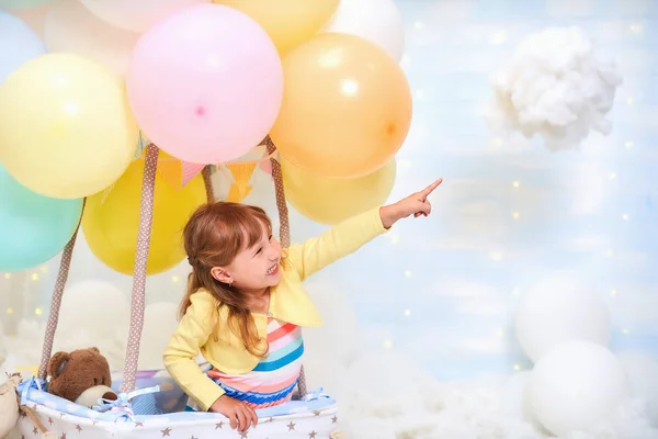 Baby girl sitting on a cloud next to a basket of balloon in the — Stock Photo, Image